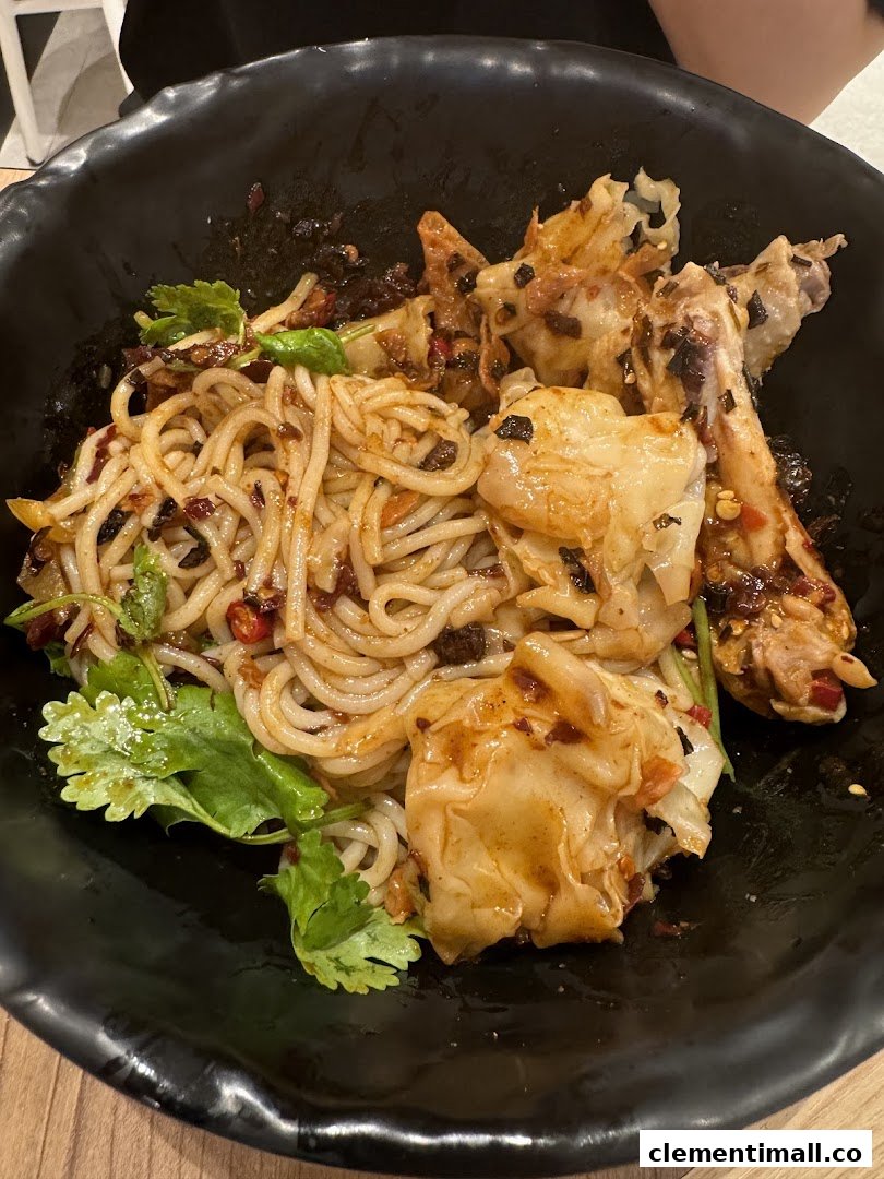 A close-up of a delicious bowl of spicy noodles with dumplings and chicken in a black bowl.