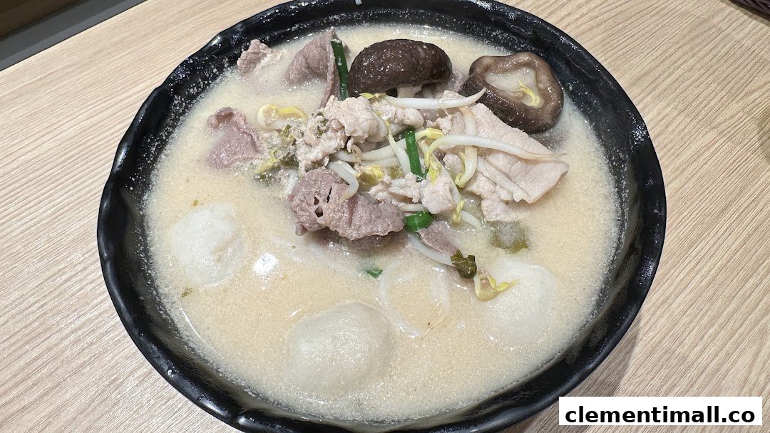 A close-up of a bowl of TamJai SamGor Mixian with meat, mushrooms, and fish balls in a creamy broth.