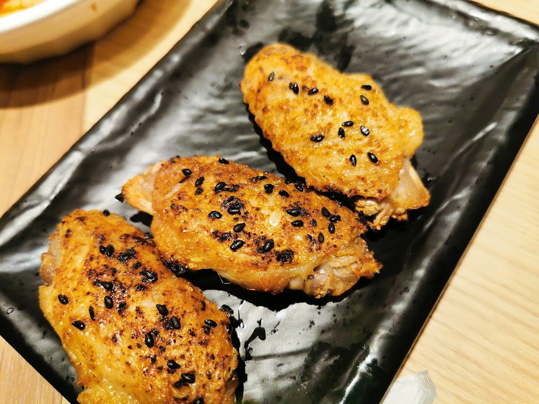 Three golden-brown chicken wings, sprinkled with black sesame seeds, served on a black rectangular plate.