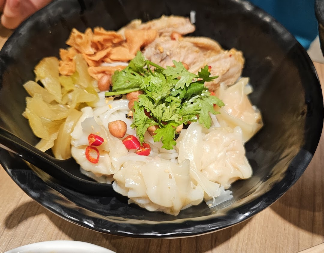 A close-up of a delicious bowl of mixian noodles with dumplings, chicken, and fresh toppings.