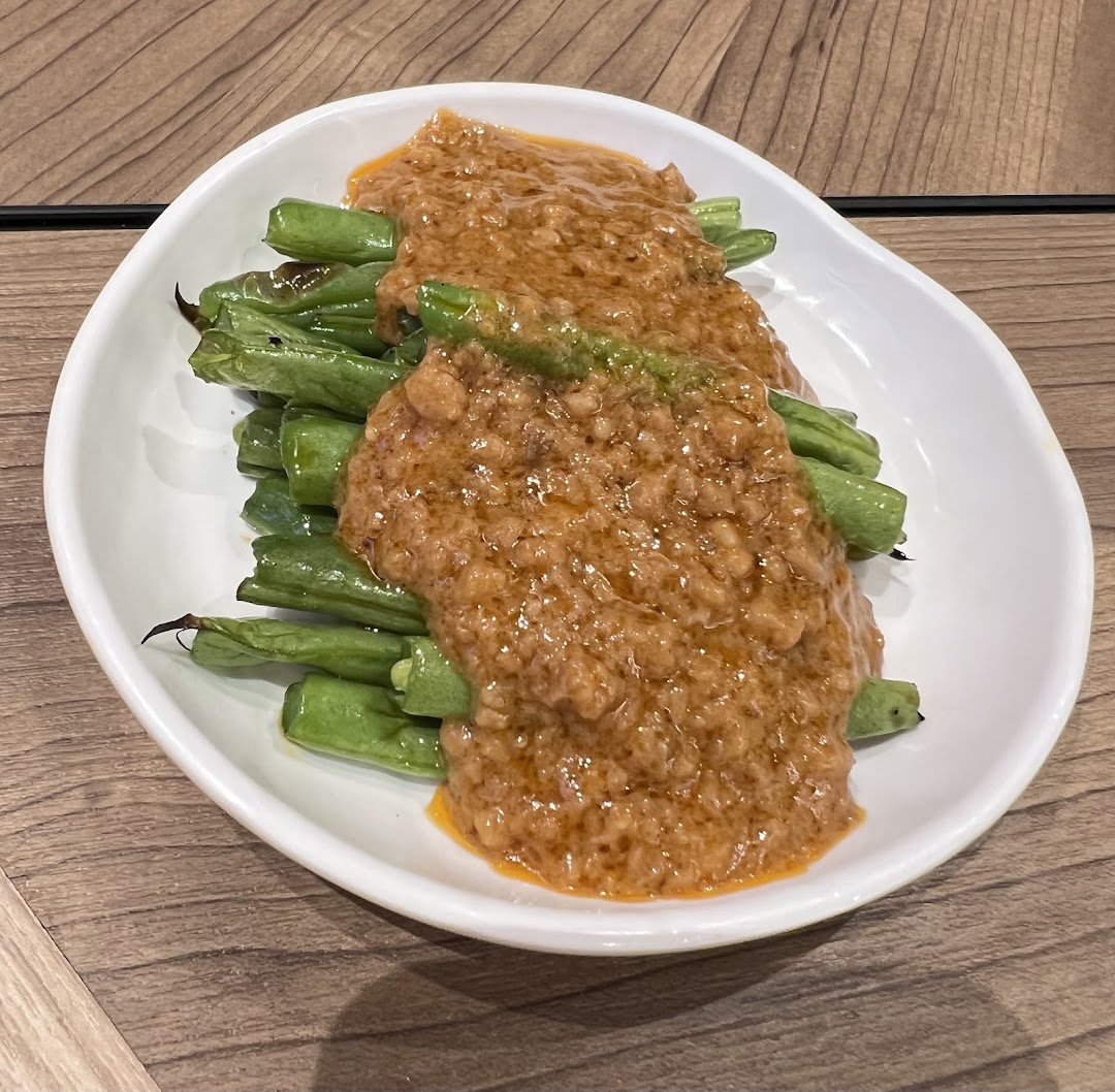 A white dish filled with green beans generously topped with a rich, savory minced meat sauce.