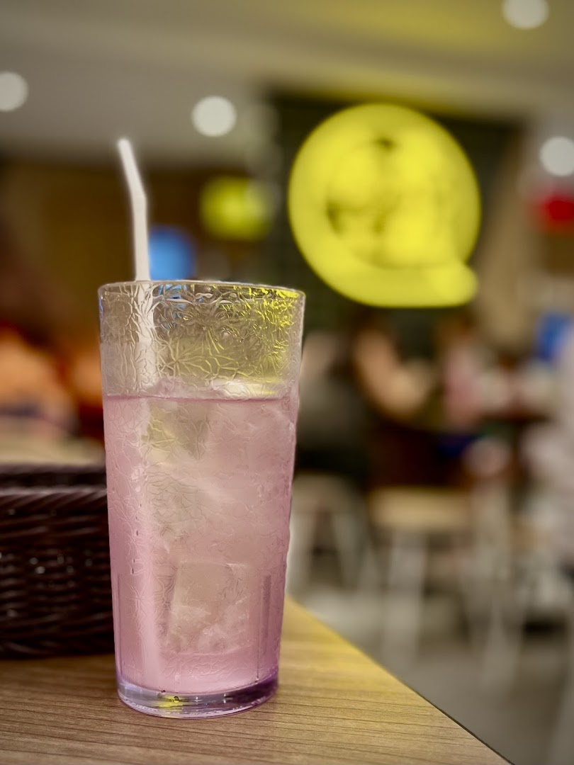 A refreshing pink drink with ice and a straw on a wooden table inside TamJai SamGor Mixian.