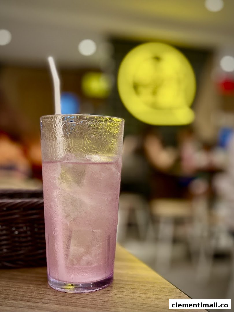 A refreshing pink drink with ice and a straw on a wooden table inside TamJai SamGor Mixian.