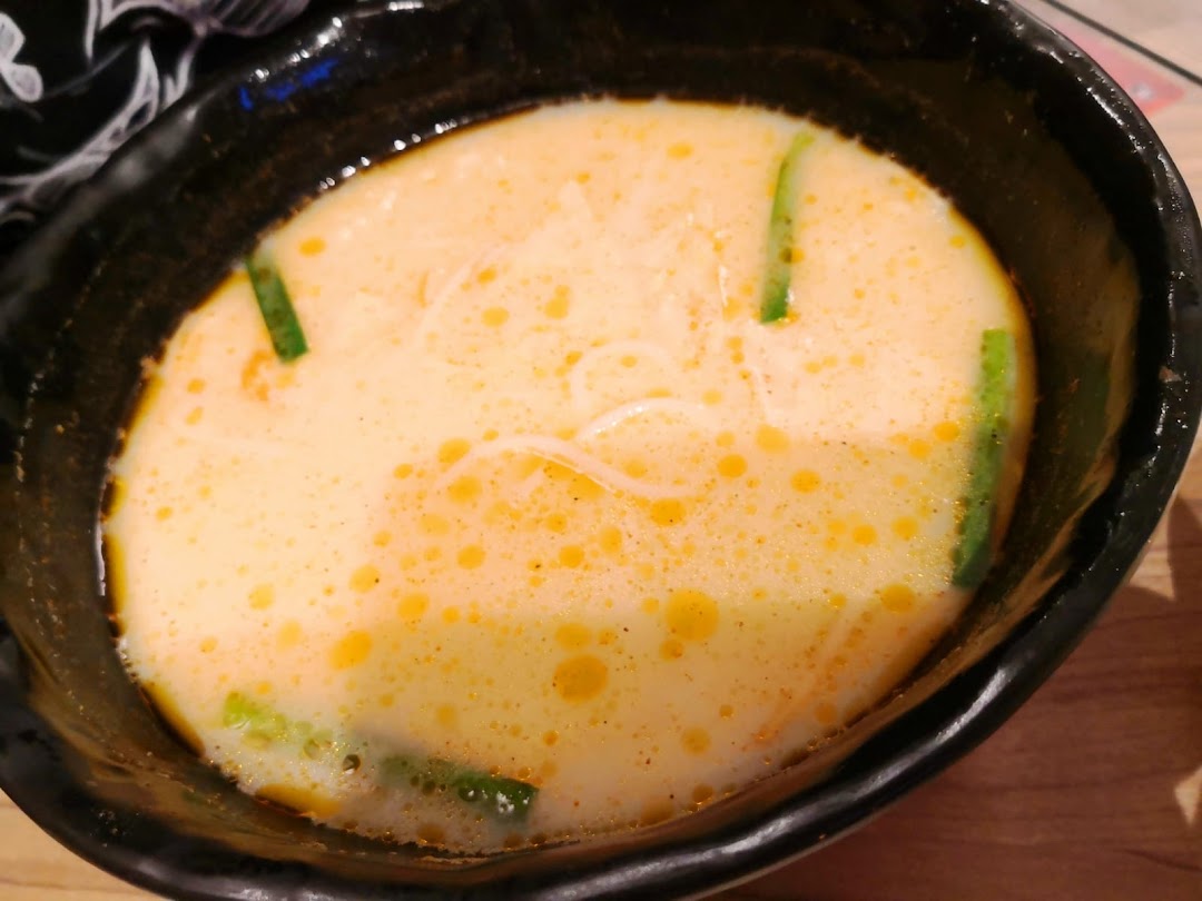A close-up of a bowl of creamy, orange-hued mixian soup with green garnishes.