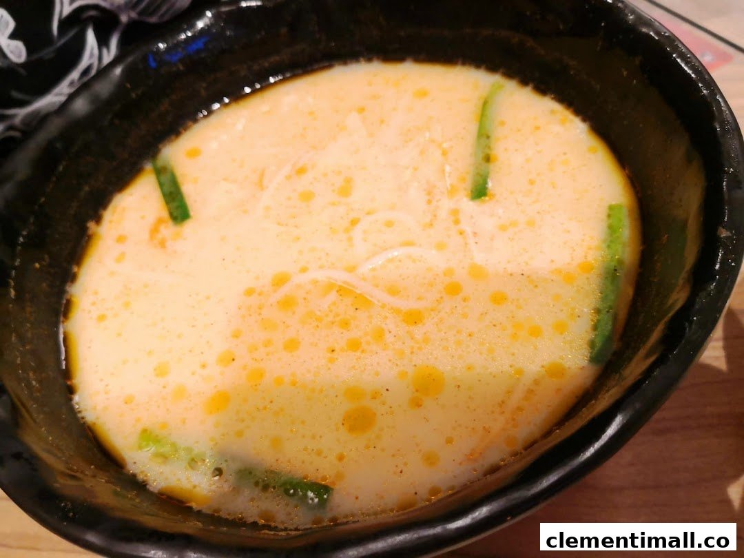 A close-up of a bowl of creamy, orange-hued mixian soup with green garnishes.