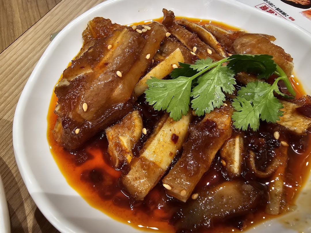 A close-up of a spicy braised dish with cilantro and sesame seeds on a white plate.