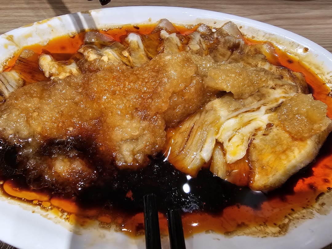 A close-up of a delicious, saucy dish, possibly a fried bean curd or meat, served in a white bowl.