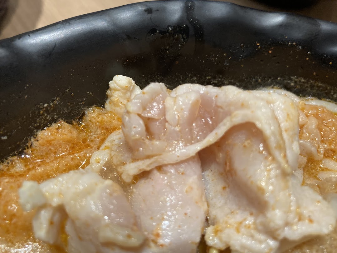 A close-up of tender meat slices in a rich, spicy broth, served in a black bowl.