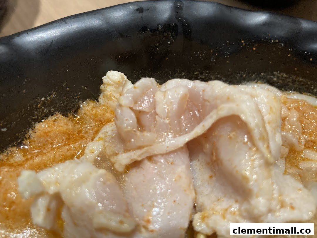 A close-up of tender meat slices in a rich, spicy broth, served in a black bowl.