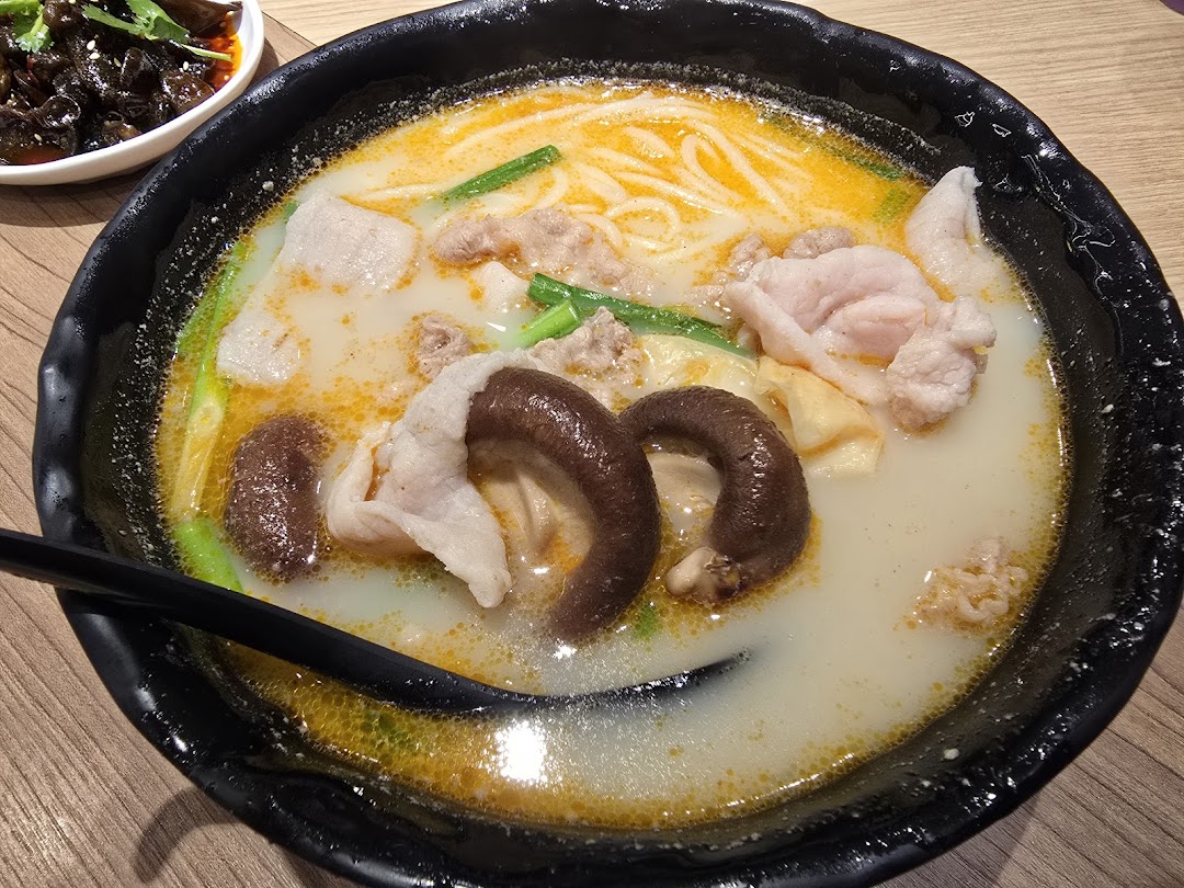 A close-up of a delicious bowl of mixian noodles with pork, mushrooms, and a rich, flavorful broth.