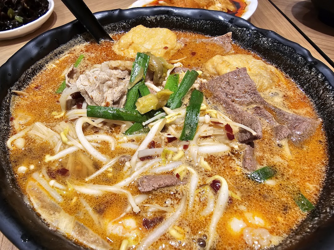 A close-up of a vibrant bowl of spicy mixian noodles with various toppings, including meat and vegetables.