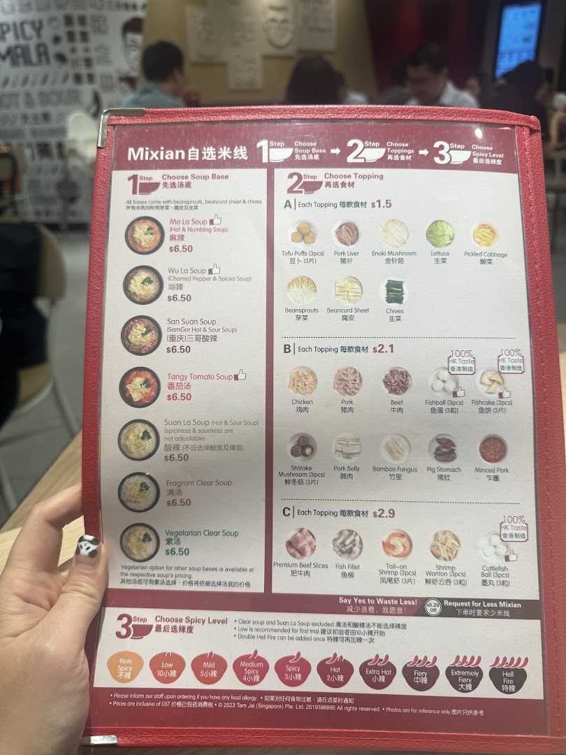 A close-up of a TamJai SamGor Mixian menu, detailing customizable soup bases, toppings, and spice levels.