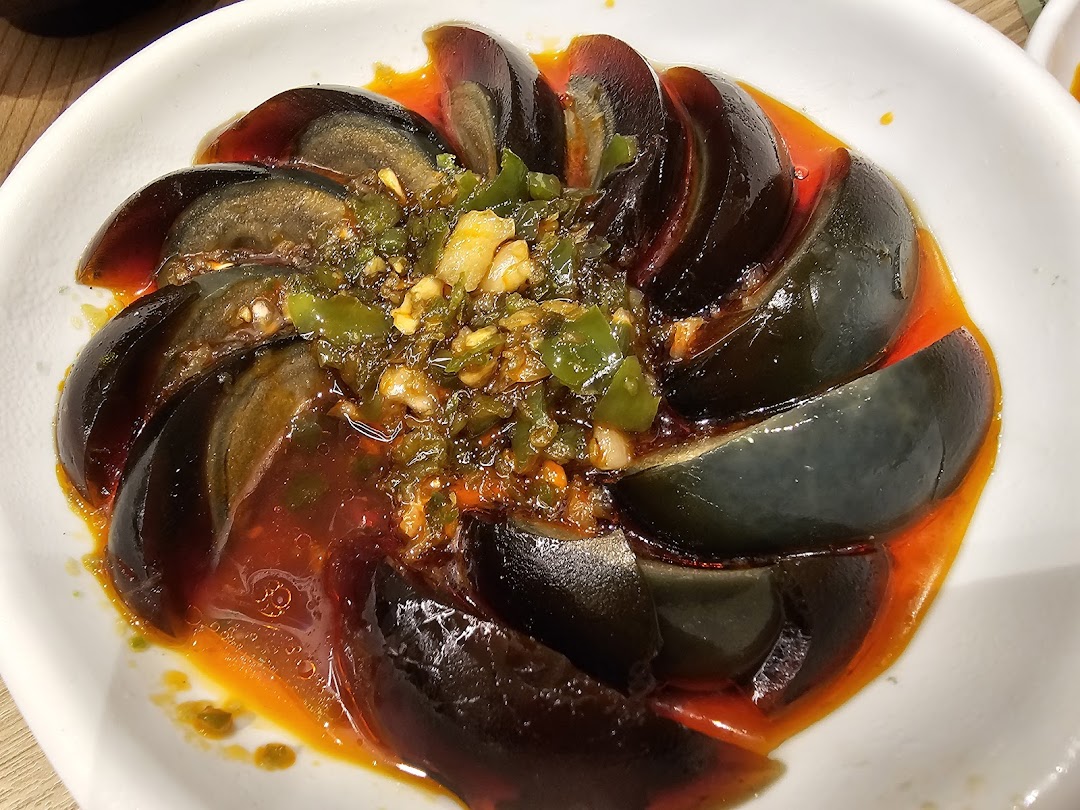 A close-up of sliced century eggs served with a vibrant spicy green chili and garlic sauce.