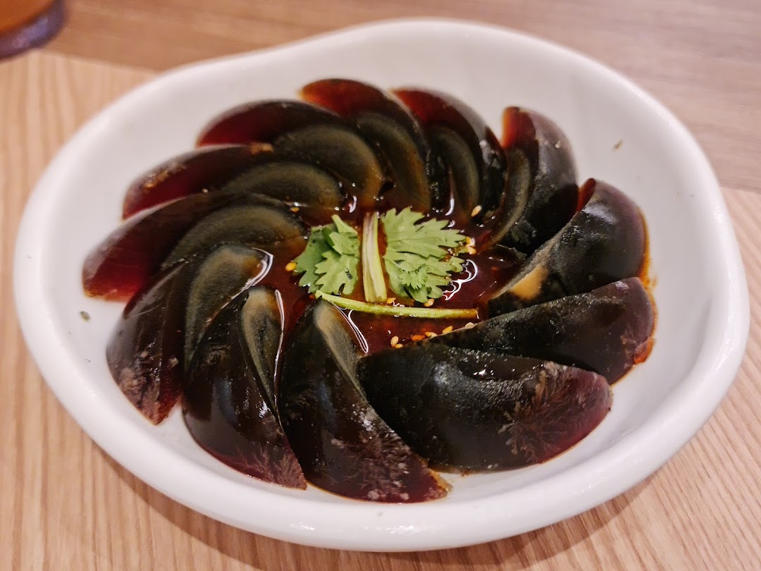 A close-up of sliced century eggs with a savory sauce and fresh cilantro in a white bowl.