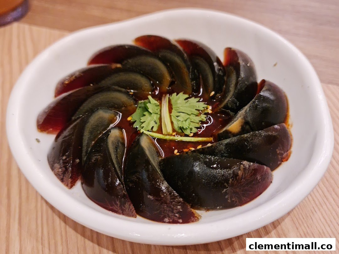 A close-up of sliced century eggs with a savory sauce and fresh cilantro in a white bowl.
