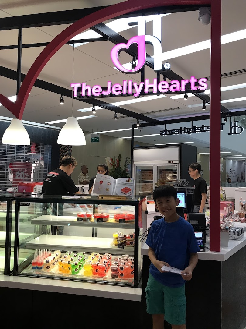 A vibrant dessert shop interior featuring colorful jelly cakes on display and a happy young customer.
