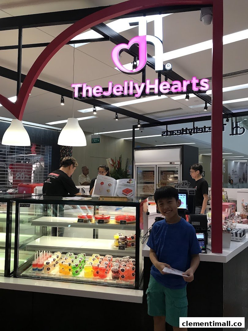 A vibrant dessert shop interior featuring colorful jelly cakes on display and a happy young customer.