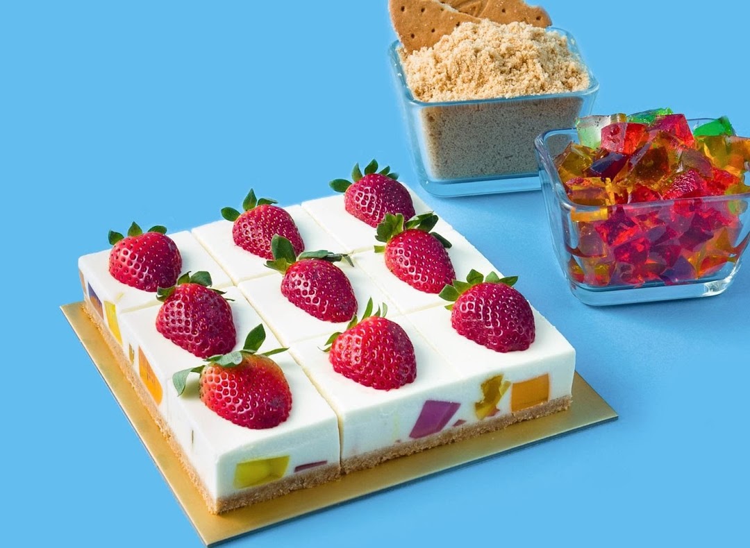 Colorful jelly cheesecake squares topped with fresh strawberries, with ingredients nearby.