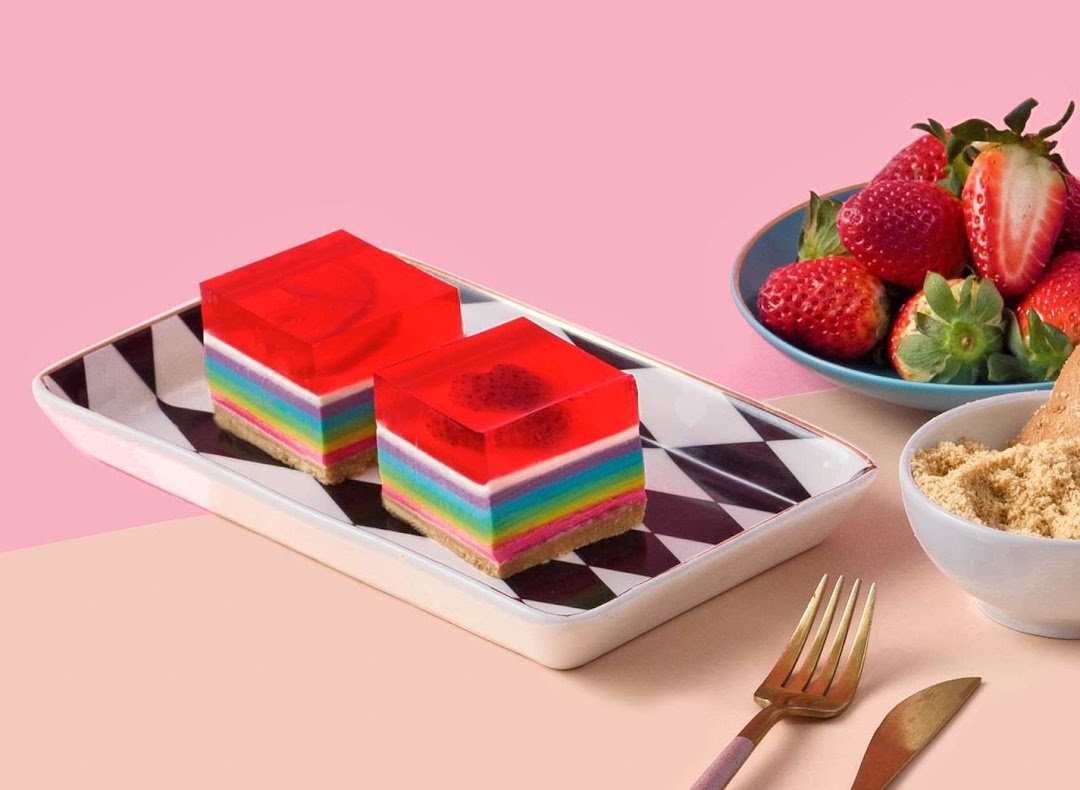 Two vibrant rainbow jelly cakes with fresh strawberries on a checkered plate.