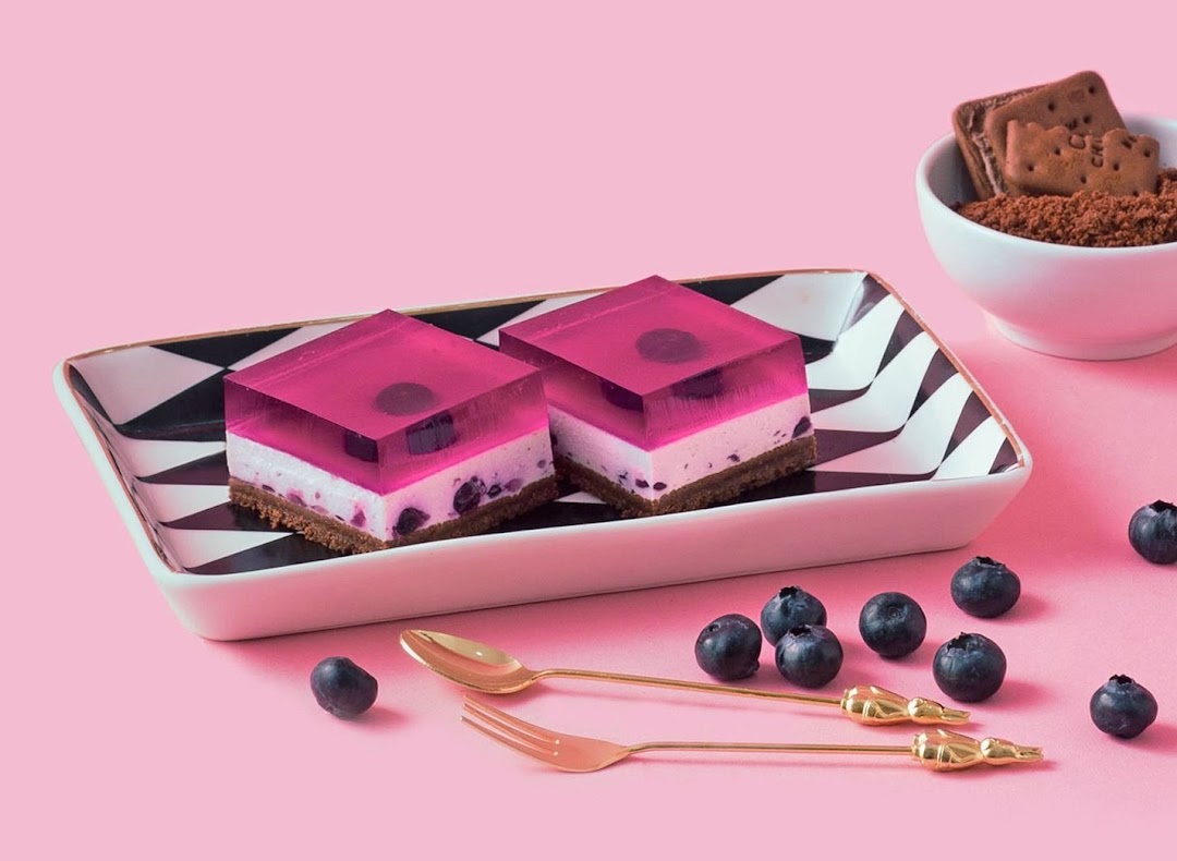 Two vibrant pink jelly desserts with blueberry and cream layers on a decorative plate.