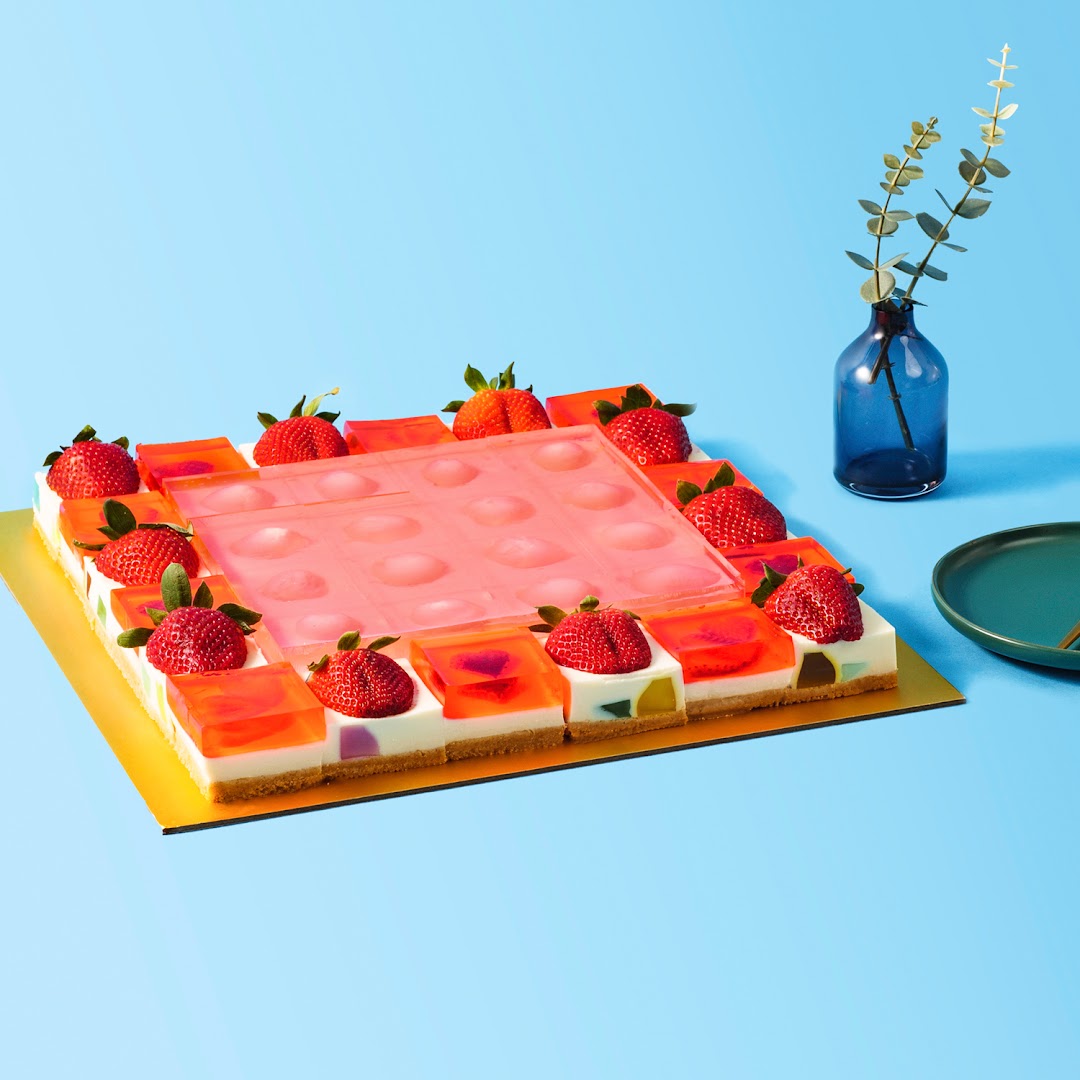 A vibrant, square jelly cake adorned with fresh strawberries on a bright blue background.