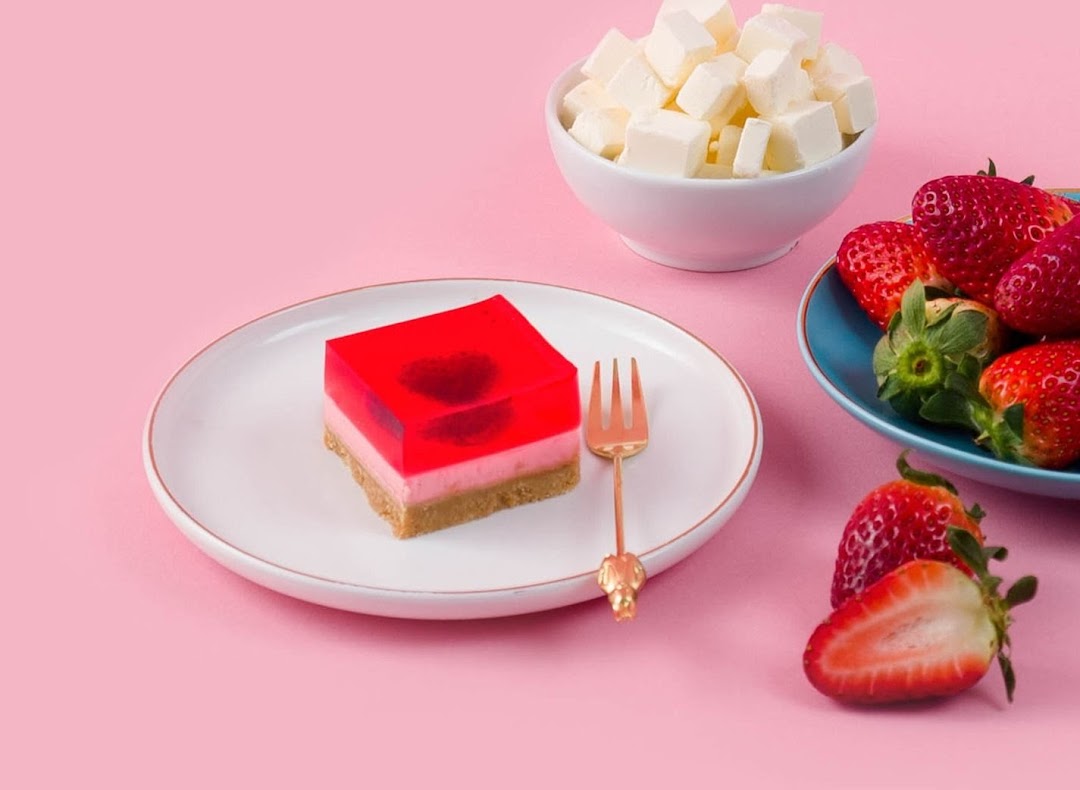 A vibrant red jelly dessert with a heart design, served with fresh strawberries and cream cheese cubes.