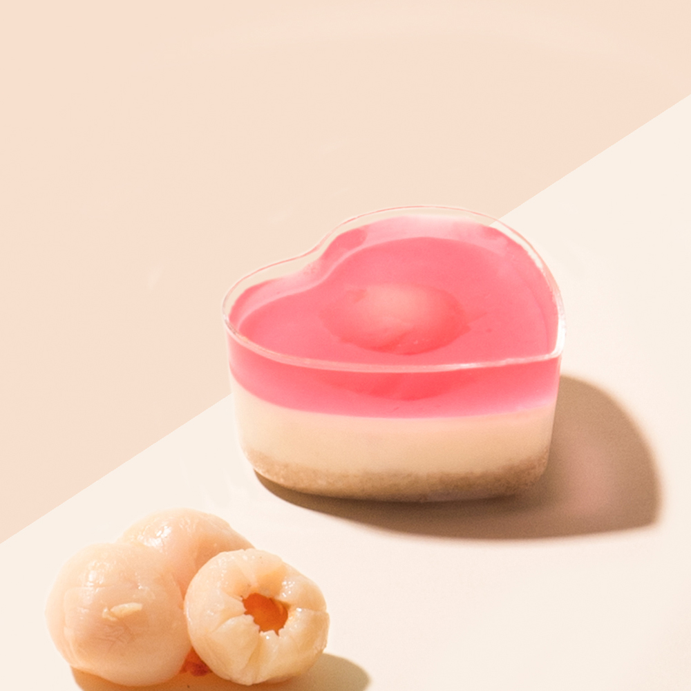 A heart-shaped dessert with pink jelly and a creamy base, accompanied by fresh lychees.