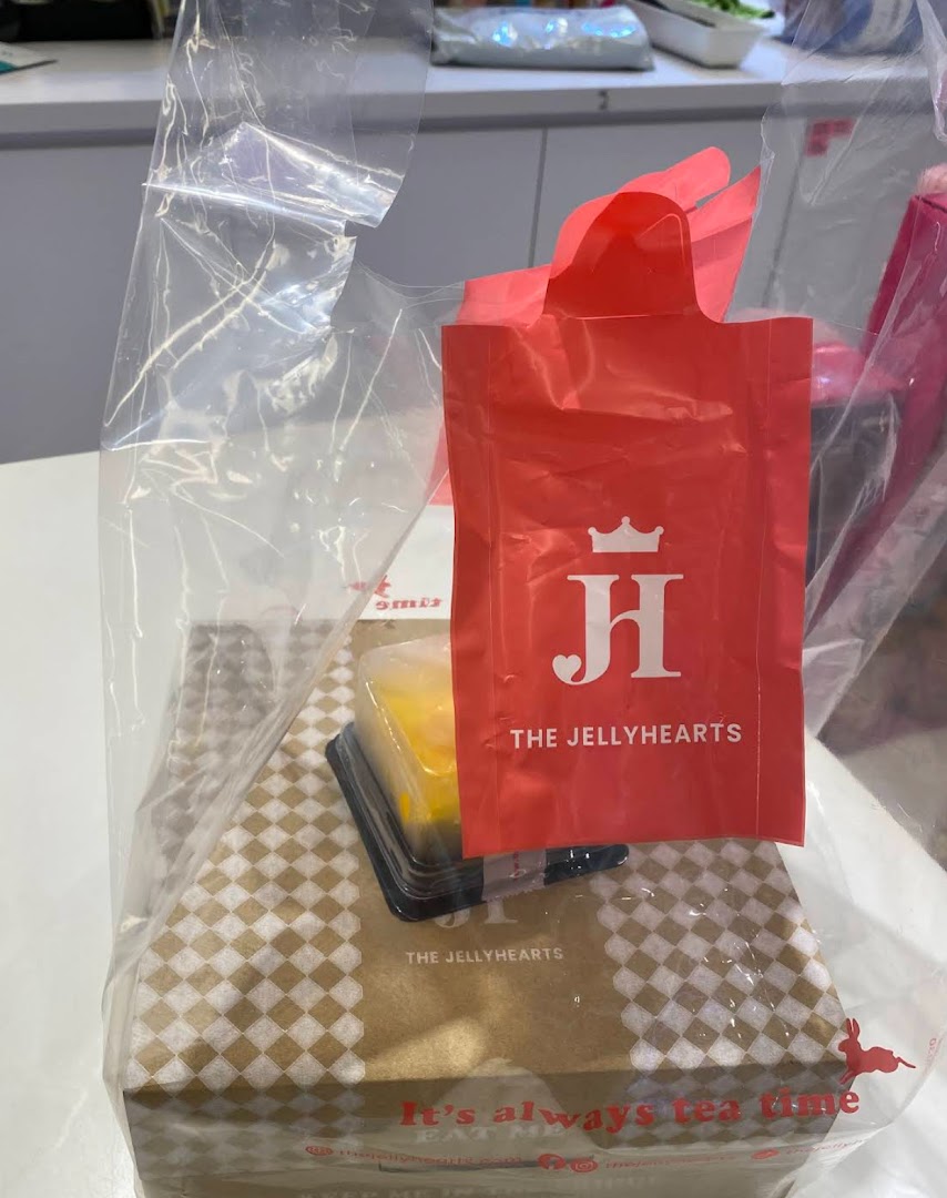 A clear plastic bag containing a branded box and a small dessert from The JellyHearts.