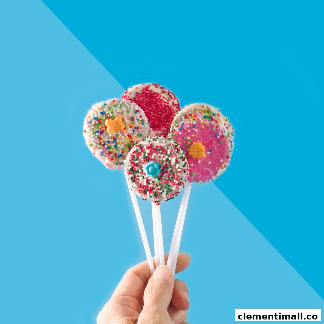 A hand holds four colorful, sprinkle-covered lollipops against a vibrant blue background.