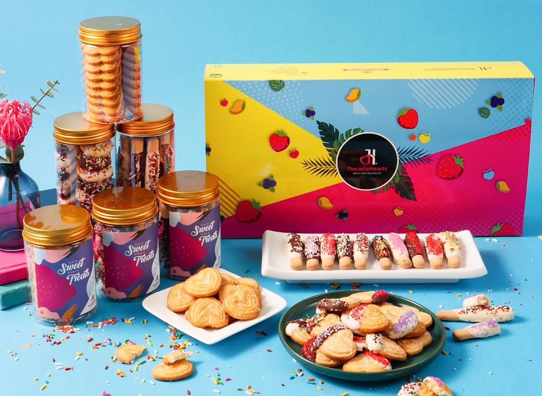 An assortment of cookies and sweet treats in jars and on plates, with a colorful gift box.