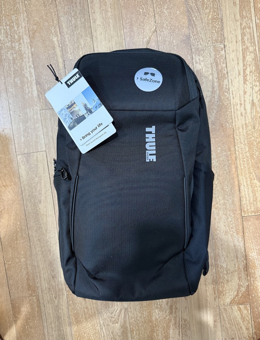 A black Thule Accent backpack with tags, featuring SafeZone protection, displayed on a wooden floor.