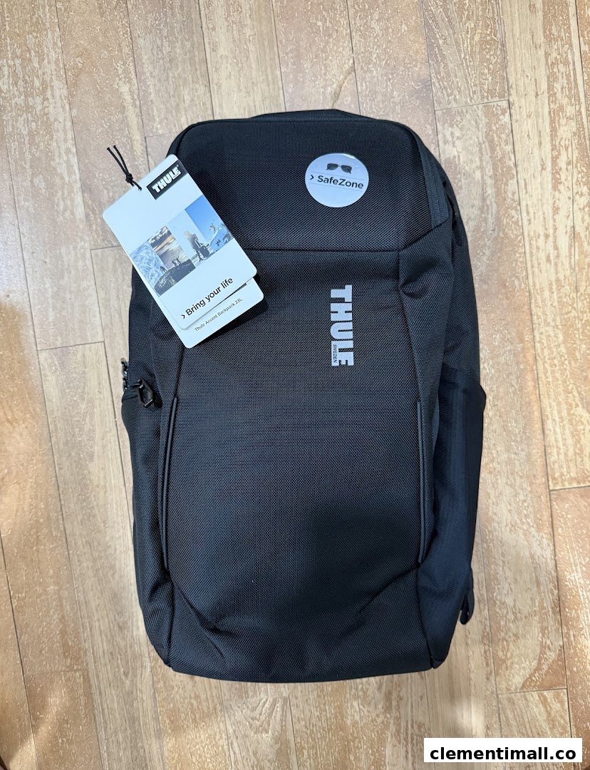 A black Thule Accent backpack with tags, featuring SafeZone protection, displayed on a wooden floor.