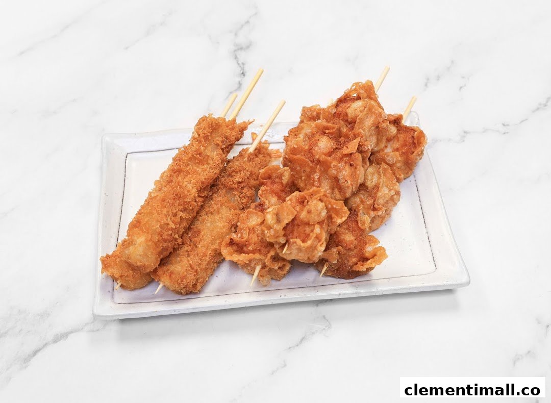 A plate of crispy fried skewers, including breaded and cornflake-crusted varieties, on a white marble background.