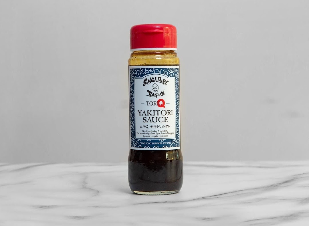 A bottle of TORI-Q Yakitori Sauce with a red cap on a marble surface.