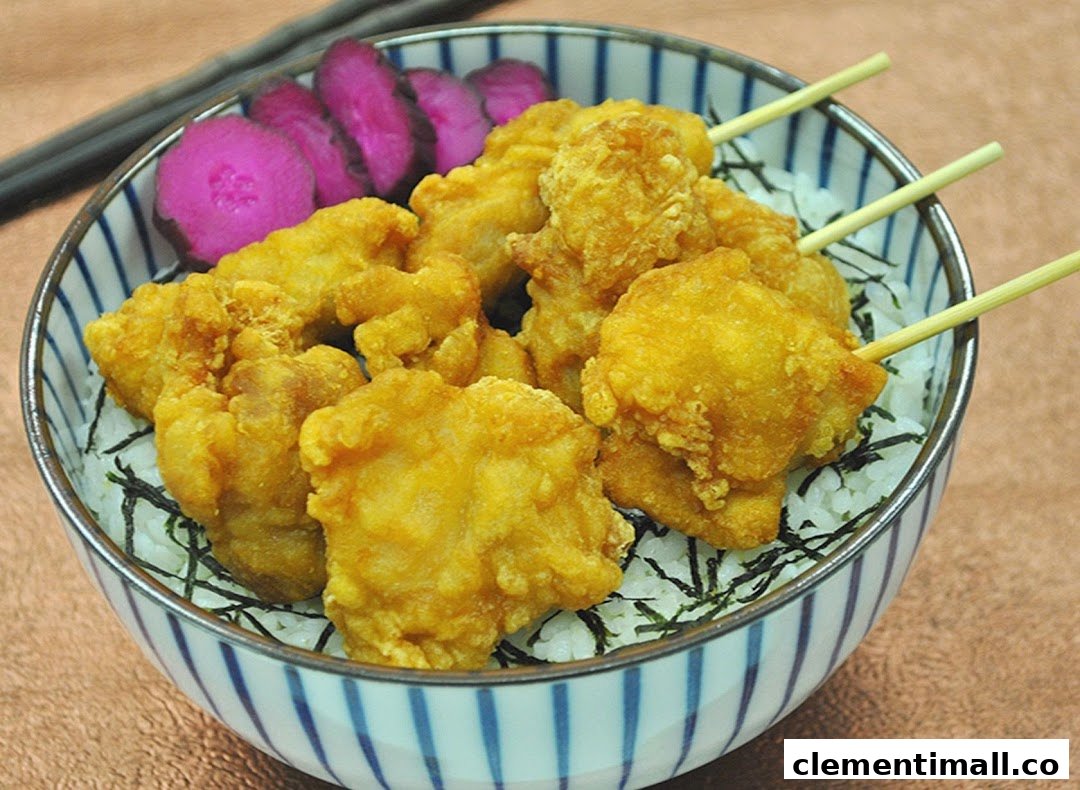A bowl of golden fried chicken pieces on rice with pickled vegetables and chopsticks.
