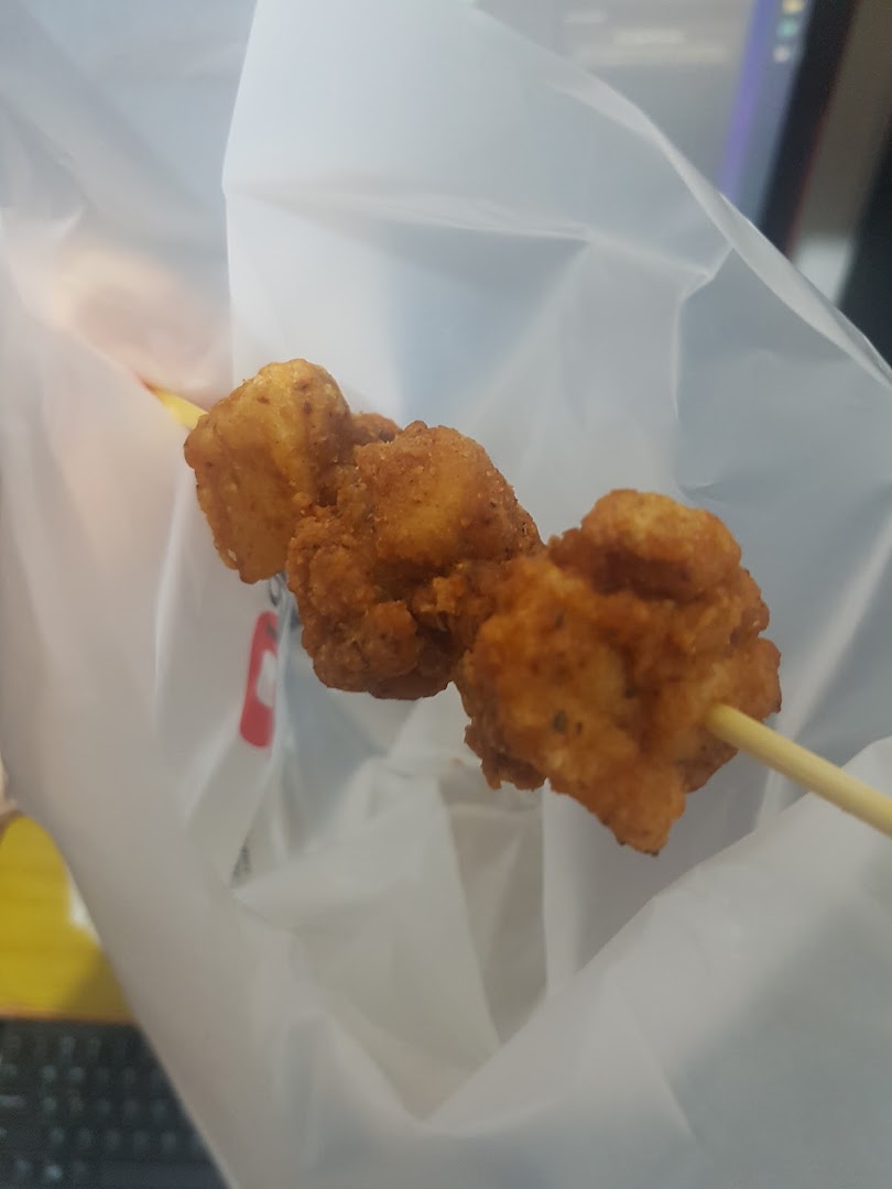 Close-up of golden-brown fried chicken pieces on a skewer, served in a white bag.
