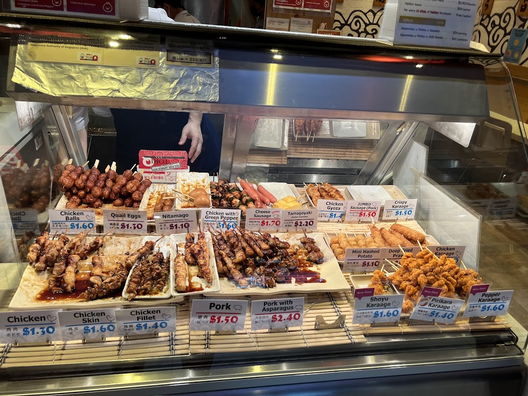 A vibrant display of Japanese skewers and fried items with prices at a food stall.