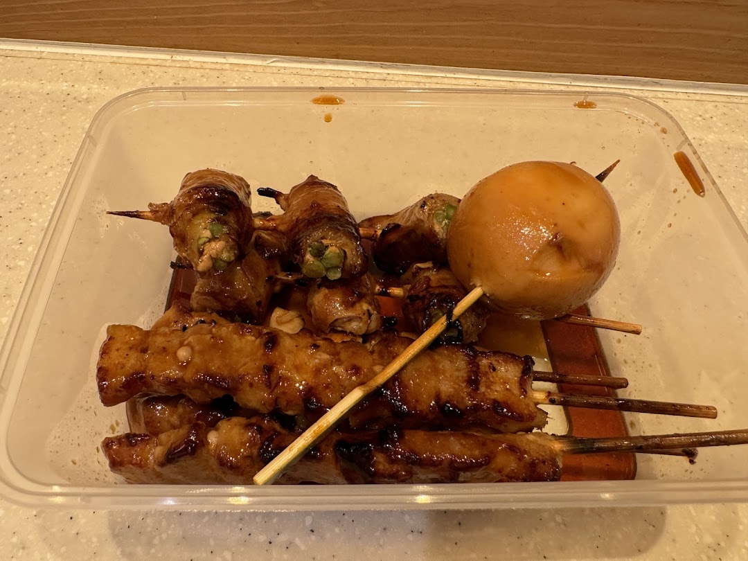 A clear container filled with various glazed skewers, including meat-wrapped vegetables and a large potato.