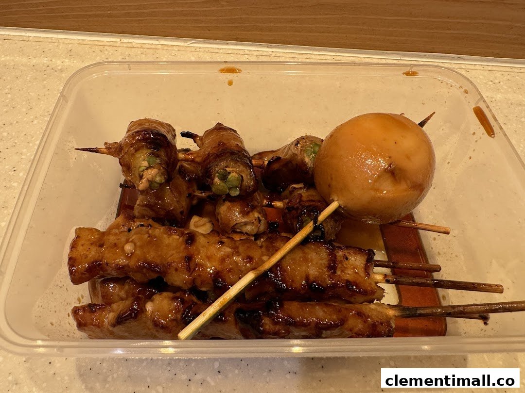 A clear container filled with various glazed skewers, including meat-wrapped vegetables and a large potato.