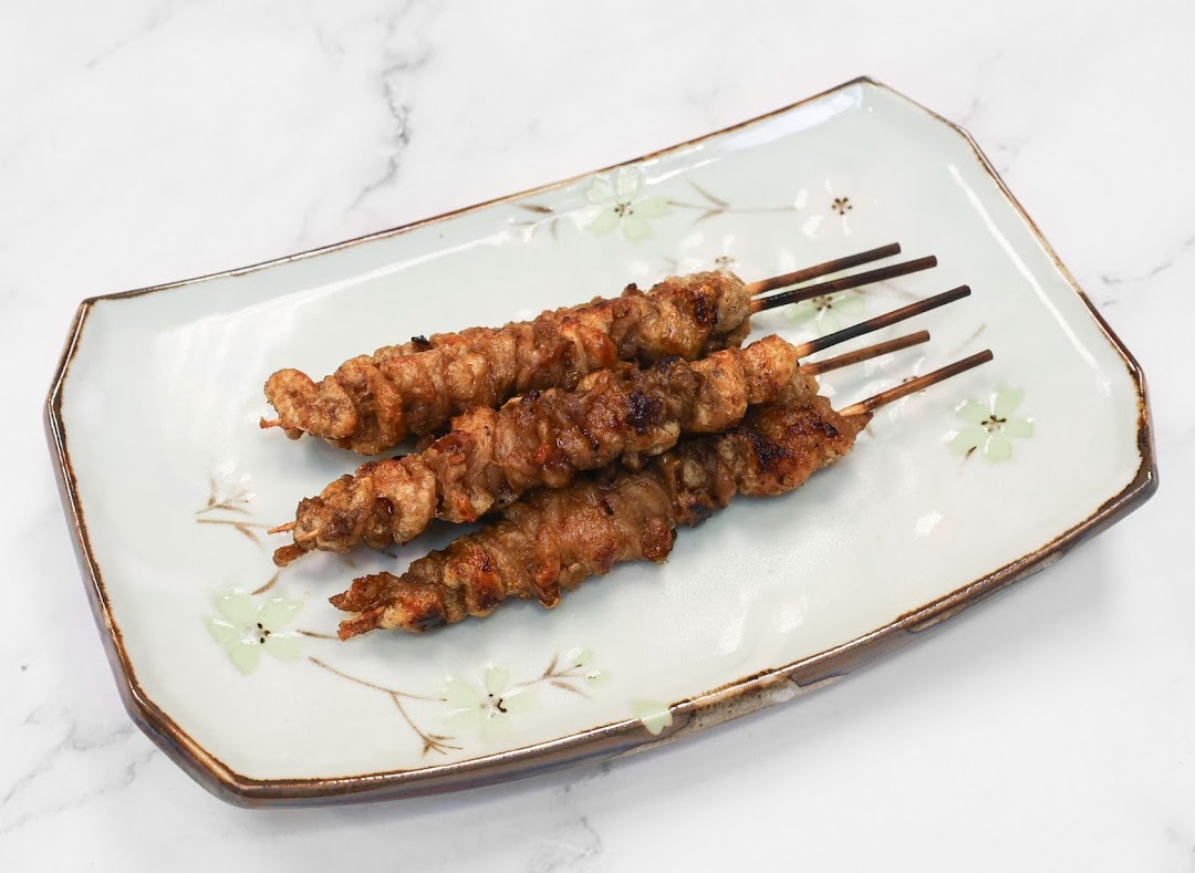 Three grilled meat skewers are presented on a decorative white plate with floral patterns.