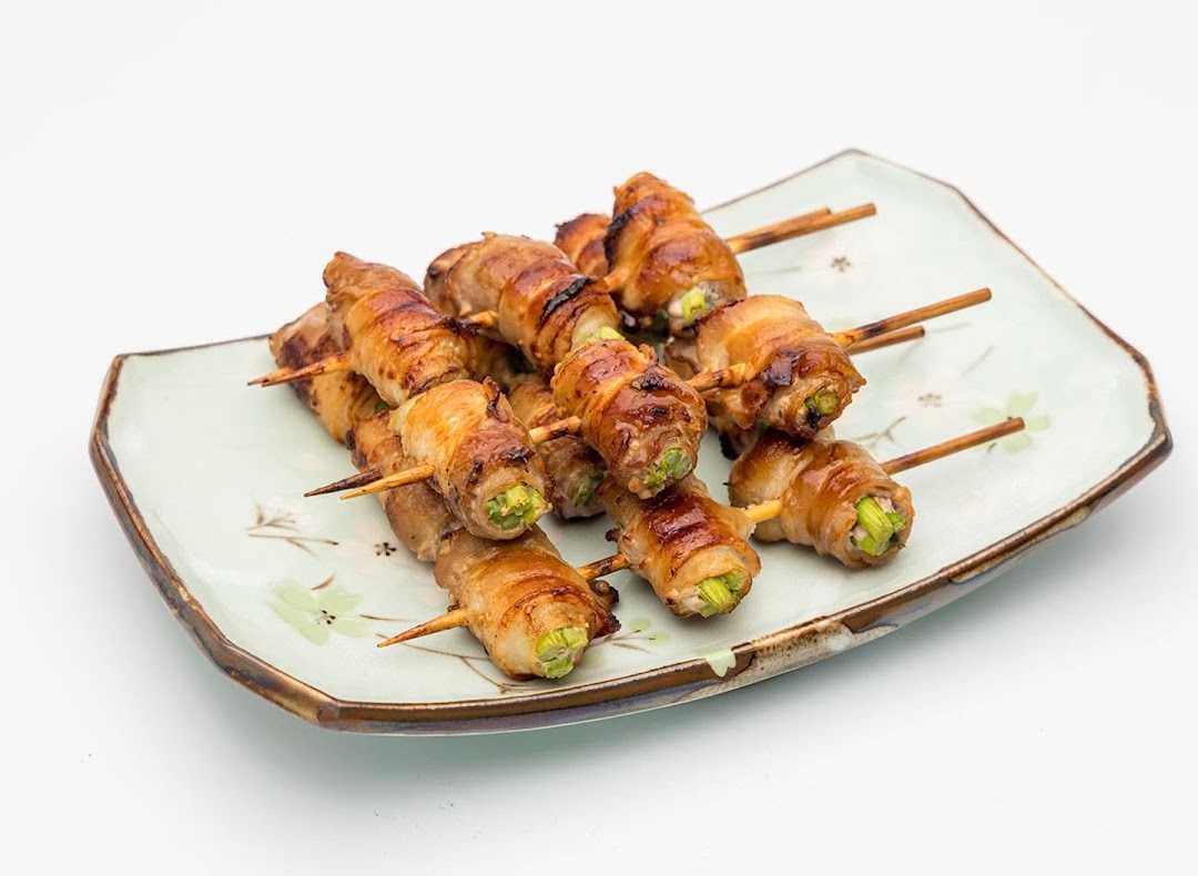 A plate of grilled skewers featuring meat-wrapped vegetables, likely yakitori, on a decorative dish.