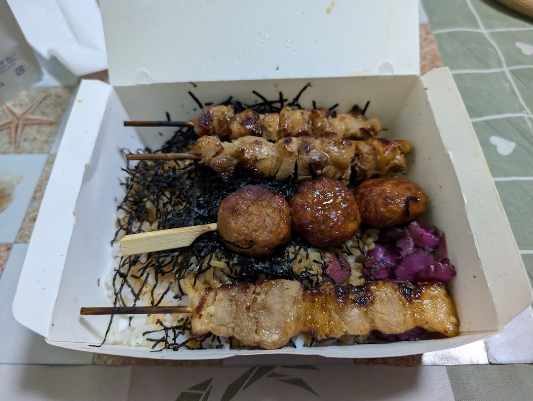 A delicious bento box featuring grilled skewers, meatballs, rice, and pickled vegetables.