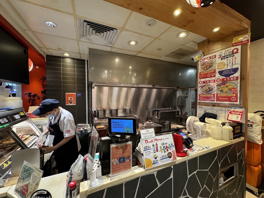 A staff member prepares food at the counter of TORI-Q, with menu boards and payment options visible.