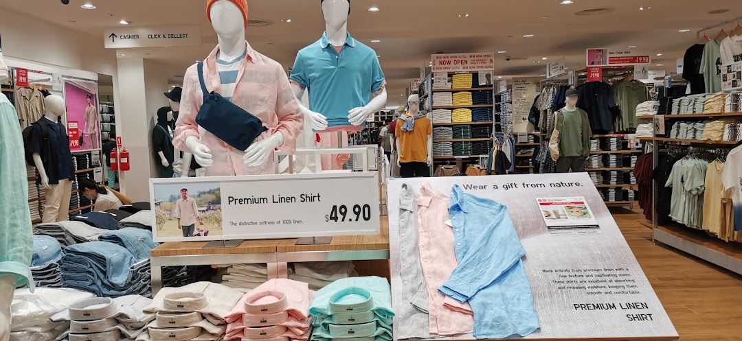 An interior view of UNIQLO, showcasing mannequins, folded apparel displays, and promotional signage for linen shirts.