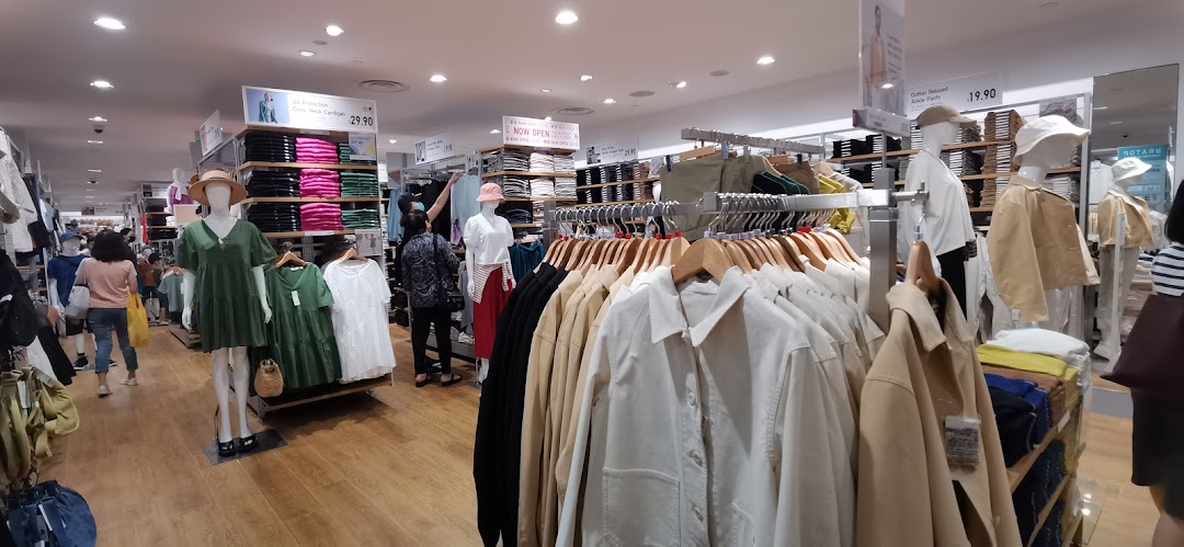 An interior view of UNIQLO, showcasing various clothing displays, mannequins, and shoppers browsing apparel.