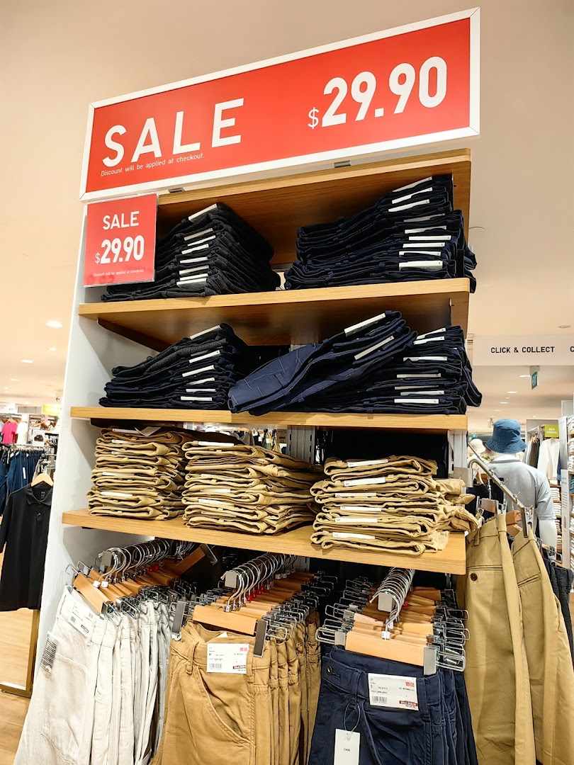 A UNIQLO store display featuring various pants on sale for $29.90.