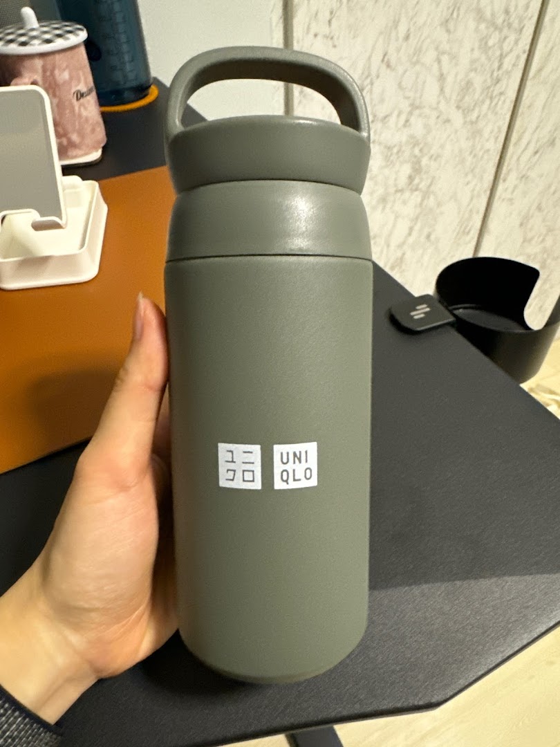 A hand holds a grey UNIQLO branded water bottle with a handle.