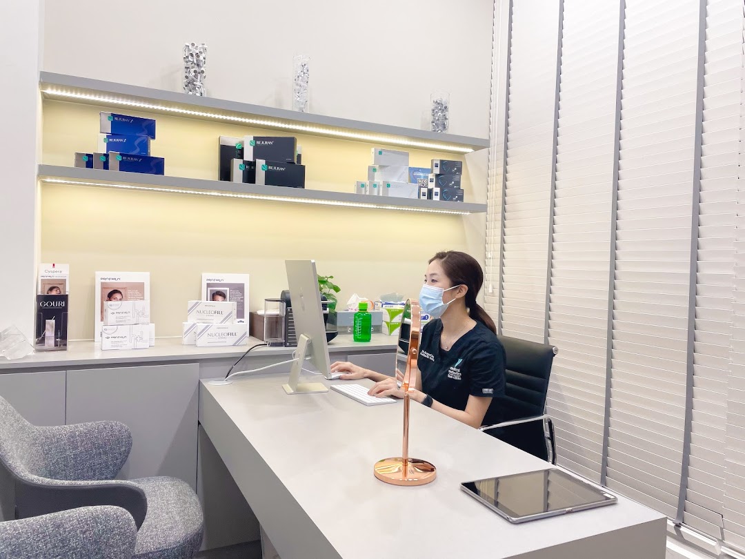 A clinic staff member at a desk with aesthetic products displayed on illuminated shelves.