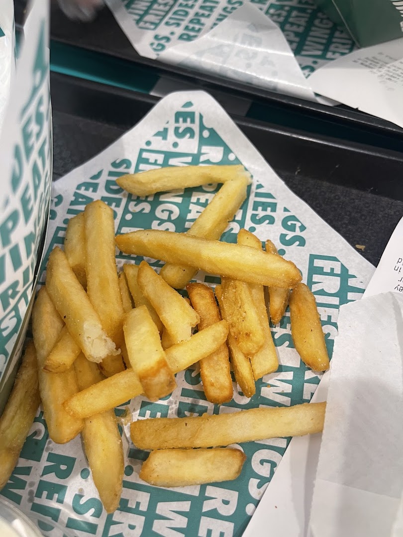 A close-up of golden fries served on Wingstop branded paper with visible branding.