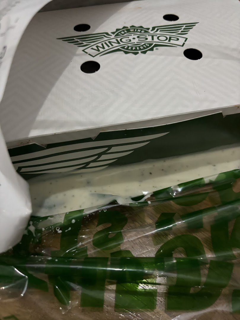 A Wingstop box with the logo visible, showing a creamy dip inside a plastic bag.